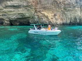 A lively group enjoys a day on the water aboard a boat near stunning cliffs, perfect for swimming and exploring the beautiful coastline.