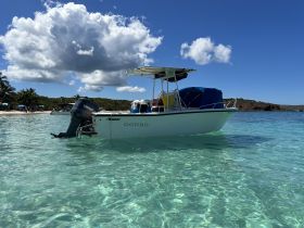 A picturesque view of the boat 'DONBO' anchored in crystal-clear waters, surrounded by lush greenery and a vibrant sky, perfect for a day of exploration.