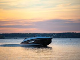 A sleek speedboat glides across the water at sunset, showcasing its elegant design against a picturesque backdrop.