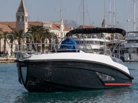 A boat navigates through a marina with a captain at the helm, showcasing the vibrant waterfront scenery and the charm of coastal life.