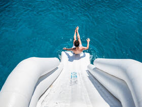A young man prepares to slide into the crystal-clear waters from an inflatable water slide, capturing the essence of summer fun and adventure on the water.