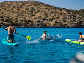 A group of friends enjoys a fun day on the water, paddleboarding and splashing around in a vibrant blue lagoon — perfect for summer adventures.