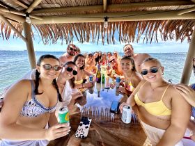 A lively group enjoys drinks and laughter under a thatched roof on a boat, capturing the essence of a fun-filled day on the water.