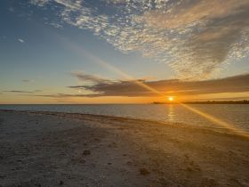 A stunning sunset over the tranquil waters, casting golden hues across the beach — a perfect backdrop for romantic evenings or peaceful reflections.