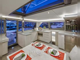 A modern and stylish interior of a boat's dining area, featuring elegant table settings and a well-equipped kitchen, perfect for entertaining guests on the water.