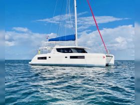 A stunning side view of a catamaran sailing through clear waters, showcasing its sleek design and vibrant sails against a picturesque sky.