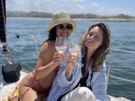 Two friends toast with cocktails aboard a sailboat, enjoying a sunny day on the water — perfect for celebrating special moments or simply relaxing with friends.