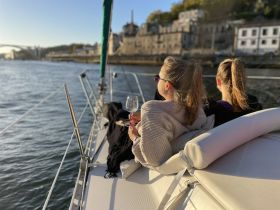 Two women enjoy a relaxing moment on a sailboat, sipping cocktails as they take in the scenic waterfront views — perfect for sunset cruises.