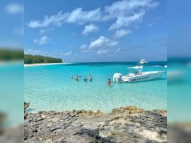 A lively group enjoys a day at the beach, wading in the crystal-clear turquoise waters with a boat anchored nearby — perfect for a fun-filled day on the water.