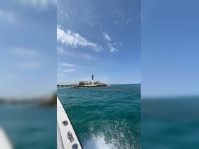 A picturesque view of a lighthouse on a small island, captured from a boat, showcasing the stunning ocean scenery and clear blue skies.
