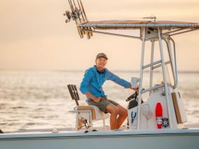 A young boy smiles while sitting at the helm of a boat, ready for a fishing adventure at sunset — a perfect moment for family outings on the water.
