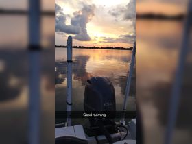 A serene morning view from a boat with a stunning sunset reflection on the water, perfect for early risers and fishing enthusiasts.