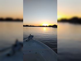A serene sunset view from the bow of a boat, showcasing calm waters and a picturesque horizon — perfect for evening cruises and relaxation on the water.