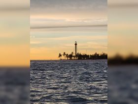 A stunning sunset view featuring a lighthouse along the coastline, creating a picturesque backdrop perfect for evening boat trips.