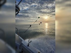 A scenic view of a boat underway at sunset, showcasing the tranquil waters and beautiful sky, perfect for fishing or leisure trips.