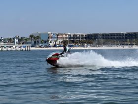A thrilling moment captured as a rider maneuvers a jet ski across the sparkling waters, with a picturesque beach and resort in the background — perfect for adventure seekers enjoying water sports.