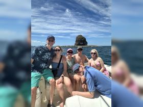 A cheerful group of friends poses for a photo on a boat, enjoying a sunny day out on the water with an island backdrop — perfect for memorable adventures and celebrations.