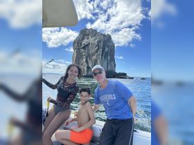 A joyful family poses on a boat with a stunning rock formation in the background, capturing a memorable day on the water.