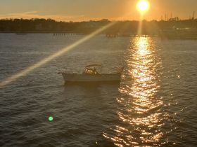 A picturesque scene of a boat silhouetted against a stunning sunset, reflecting golden hues on the water — perfect for evening cruises.