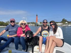 A cheerful group of friends enjoys a day on the water with their dog, posing in front of a picturesque lighthouse — perfect for memorable boating adventures.
