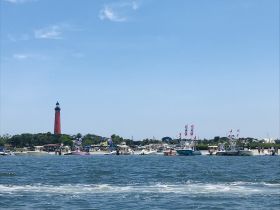 A vibrant scene featuring a red lighthouse and numerous boats gathered at the beach, showcasing a lively day on the water perfect for celebrations and gatherings.