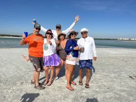 A lively group celebrates on the beach with drinks, capturing the joy of a fun day in the sun — perfect for beach parties and gatherings.