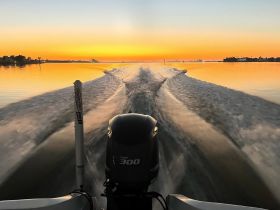 A stunning view from the back of a boat, showcasing the wake against a vibrant sunset backdrop — perfect for capturing the essence of a serene evening on the water.