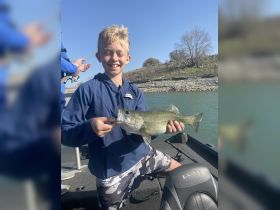 A young boy proudly holds up a freshly caught bass while fishing on a boat, capturing the joy of a successful day on the water.