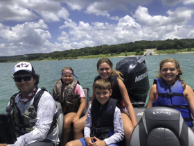 A joyful group of children and an adult enjoy a sunny day on a boat at the lake, showcasing the fun of family outings on the water.