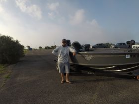 A man stands next to a Lund fishing boat parked on a launch ramp, showcasing the boat's sleek design and readiness for a day on the water.