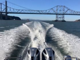 A dynamic view from the back of a boat cruising through a waterway, showcasing the impressive bridge structure above — a perfect representation of adventure on the water.