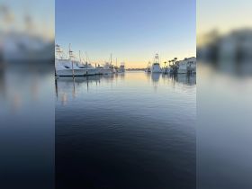A serene view of a marina at sunset, showcasing various yachts docked peacefully along the water's edge — perfect for boating enthusiasts and sunset lovers.
