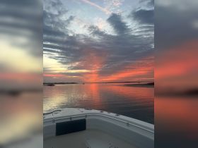A serene sunset view from the deck of a boat, showcasing vibrant colors reflecting on calm waters — perfect for peaceful evening cruises.