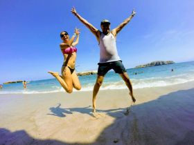 A joyful couple leaps in the air on a sunny beach, capturing the essence of fun and celebration during their seaside adventure.