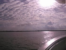 A serene view of the water reflecting sunlight under a dramatic sky, showcasing the peaceful ambiance of a boating experience.