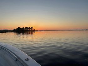 A serene sunset view from the edge of a boat, showcasing tranquil waters and a distant island silhouette — perfect for peaceful evening cruises.