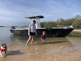 A family enjoys a fun day at the beach with their dog, playing in the shallow water next to their boat, 'Everett's Adventure.' Perfect for memorable family outings on the water.