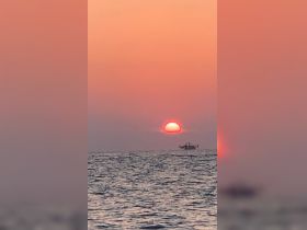 A serene sunset view featuring a boat silhouetted against the vibrant sky, perfect for capturing the tranquility of evening on the water.