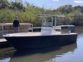 A man stands beside a sleek fishing boat at the dock, ready for a day on the water. This scene captures the anticipation of a fishing adventure in a serene setting.