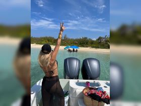 A woman joyfully waves from the boat while friends enjoy a sunny day at the beach, creating a perfect backdrop for fun and relaxation in the water.