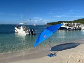 A group enjoys a sunny day at the beach with boats anchored nearby, perfect for fishing and relaxation in the clear waters.