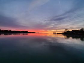 A stunning sunset casts vibrant colors across the water, creating a serene reflection along the coastline — perfect for capturing the beauty of nature.