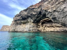 A stunning view of a rocky coastline with a cave, showcasing the beautiful turquoise waters — perfect for exploring hidden gems during a boat trip.