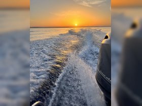 A stunning sunset view from a boat, showcasing the shimmering water and wake as the sun dips below the horizon — perfect for capturing the essence of a serene evening on the water.