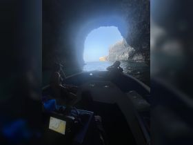 Guests relax on a boat while exploring a stunning cave entrance, showcasing the beauty of nature and adventure on the water.