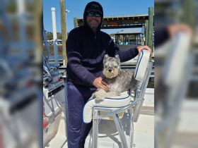 A smiling captain enjoys a moment with his dog aboard a boat, showcasing the joy of companionship on the water.