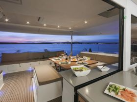 An elegant dining area inside a yacht, featuring a beautifully set table with delicious meals and a stunning view of the ocean at sunset — perfect for intimate gatherings or sunset dinners on the water.