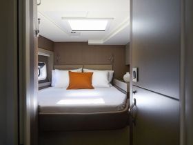 A cozy cabin interior featuring a comfortable bed with an orange accent pillow, perfect for relaxing on a boat getaway.