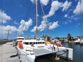 A catamaran named 'Sandstar' docked at a marina under a bright blue sky, showcasing its sleek design and vibrant kayaks on the deck.