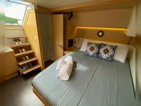 A cozy cabin interior featuring a comfortable bed with decorative pillows and neatly rolled towels, perfect for relaxation during a boating adventure.